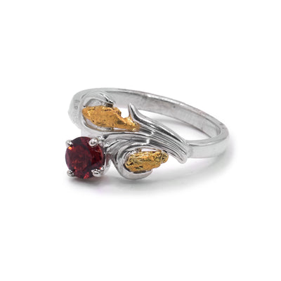 This garnet solitaire ring has a thin, sterling silver band that has wavy shapes at the top of it. These wavy designs depict a floral shape with a garnet gem and two 22K gold nuggets held in the curves of the band.