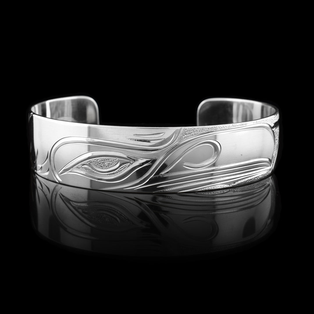 These Raven cuff bracelets have single, sterling silver bands with a gap in the back of them. There is a depiction of the head of the Raven carved across the front of the band at a side profile. There are wings with feather designs carved into both ends of the piece.