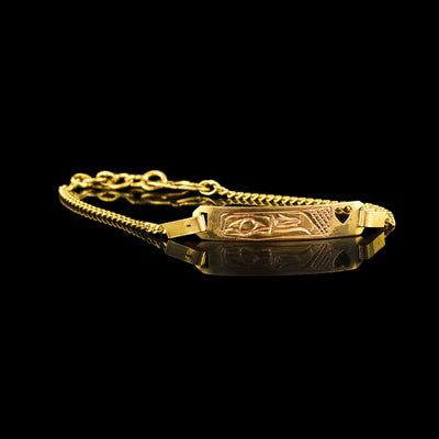 This dainty gold bracelet is made from 18K gold and has dainty chain made from small, square links. There is a flat piece in the middle of the chain with a depiction of the Eagle carved into it. The head of the Eagle is shown at a side profile on the bar.