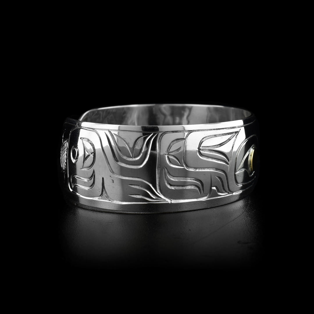 This Wolf cuff bracelet has a single, wide band made from sterling silver. There is a depiction of the Wolf legend carved at a side profile into the band. The wolfs eye is made using 14K gold.