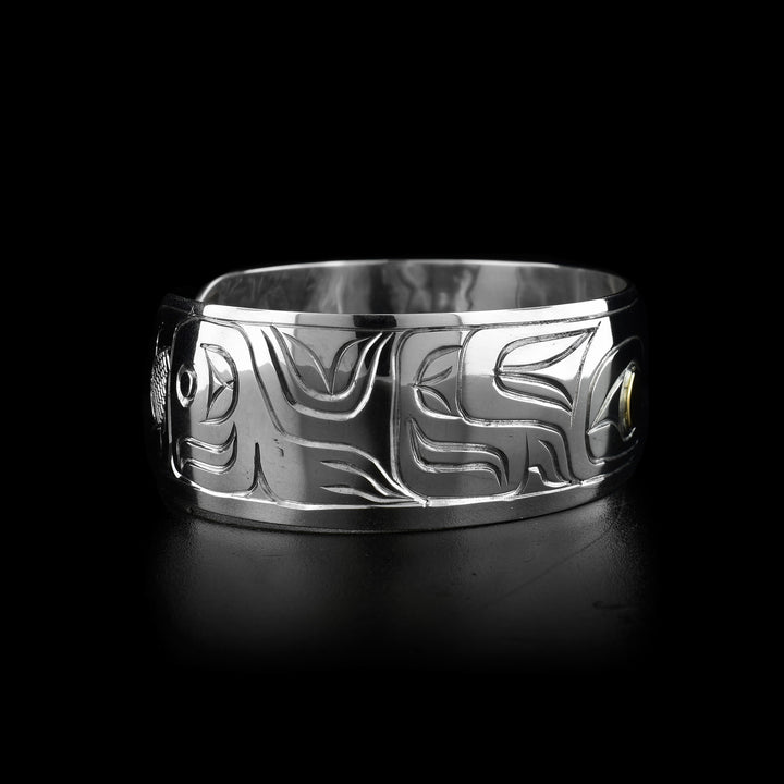 This Wolf cuff bracelet has a single, wide band made from sterling silver. There is a depiction of the Wolf legend carved at a side profile into the band. The wolfs eye is made using 14K gold.