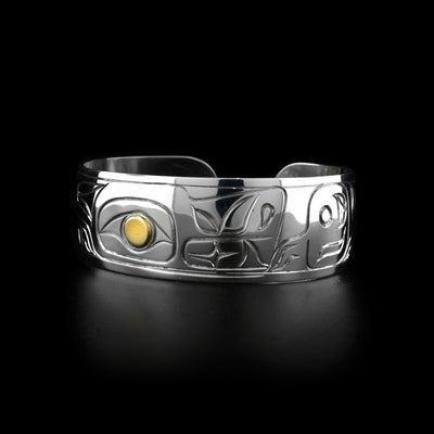 This Wolf cuff bracelet has a single, wide band made from sterling silver. There is a depiction of the Wolf legend carved at a side profile into the band. The wolfs eye is made using 14K gold.