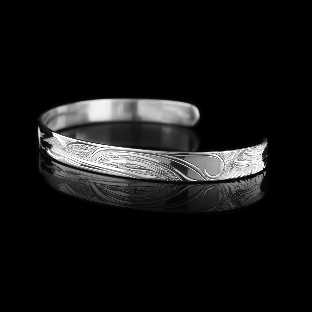 This Hummingbird and Orca bracelet has a single, sterling silver band with a gap in the back. The head of the Hummingbird is on one side of the band and the Orca's head on the other. The legends are facing each other and there is a wing design behind the hummingbird.