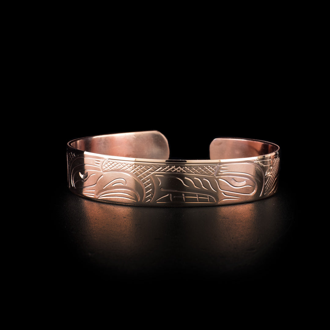 This copper cuff bracelet has a single band with a gap in the back. There are depictions of the Eagle and Wolf legends and their heads meet at the front of the band. Their bodies stretch across the rest of the band and there are cross hatching patterns in the negative spaces of the scene.