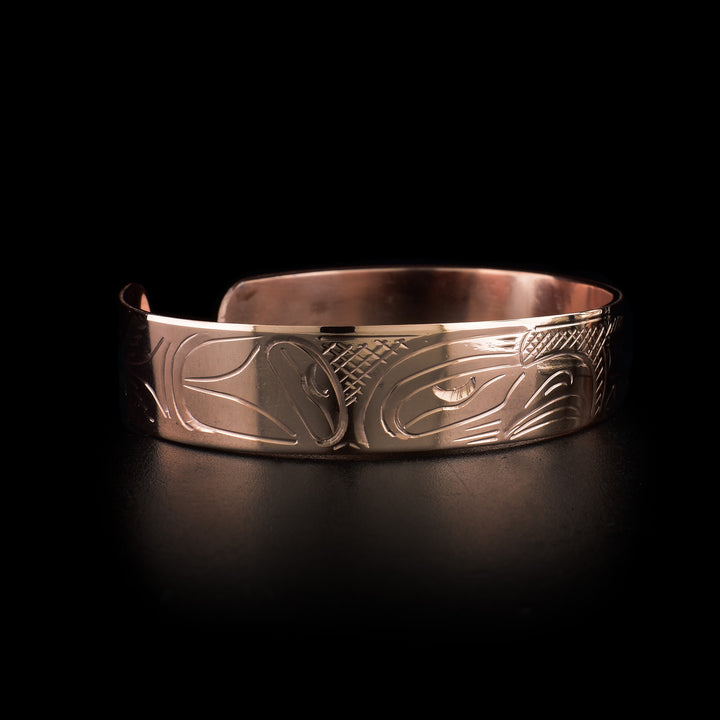 This copper cuff bracelet has a single band with a gap in the back. There are depictions of the Eagle and Wolf legends and their heads meet at the front of the band. Their bodies stretch across the rest of the band and there are cross hatching patterns in the negative spaces of the scene.