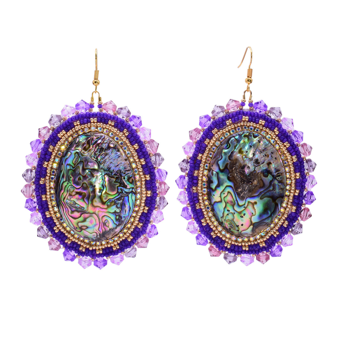 These dangling beaded earrings have large, oval shaped abalone hangs with chromatic colours on the surface of them. There are purple beads woven into a pattern around the outside of the piece. There are small, gold beads lining the circumference of the abalone and larger beads on the very outside of the hangs.