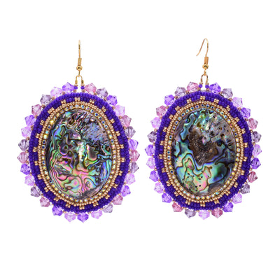 These dangling beaded earrings have large, oval shaped abalone hangs with chromatic colours on the surface of them. There are purple beads woven into a pattern around the outside of the piece. There are small, gold beads lining the circumference of the abalone and larger beads on the very outside of the hangs.