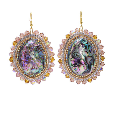 These dangling beaded earrings have large, oval shaped abalone hangs with chromatic colours on the surface of them. There are different coloured gold beads and clear highlight beads woven into a pattern around the outside of the piece. There are small beads lining the circumference of the abalone and larger beads on the very outside of the hangs.