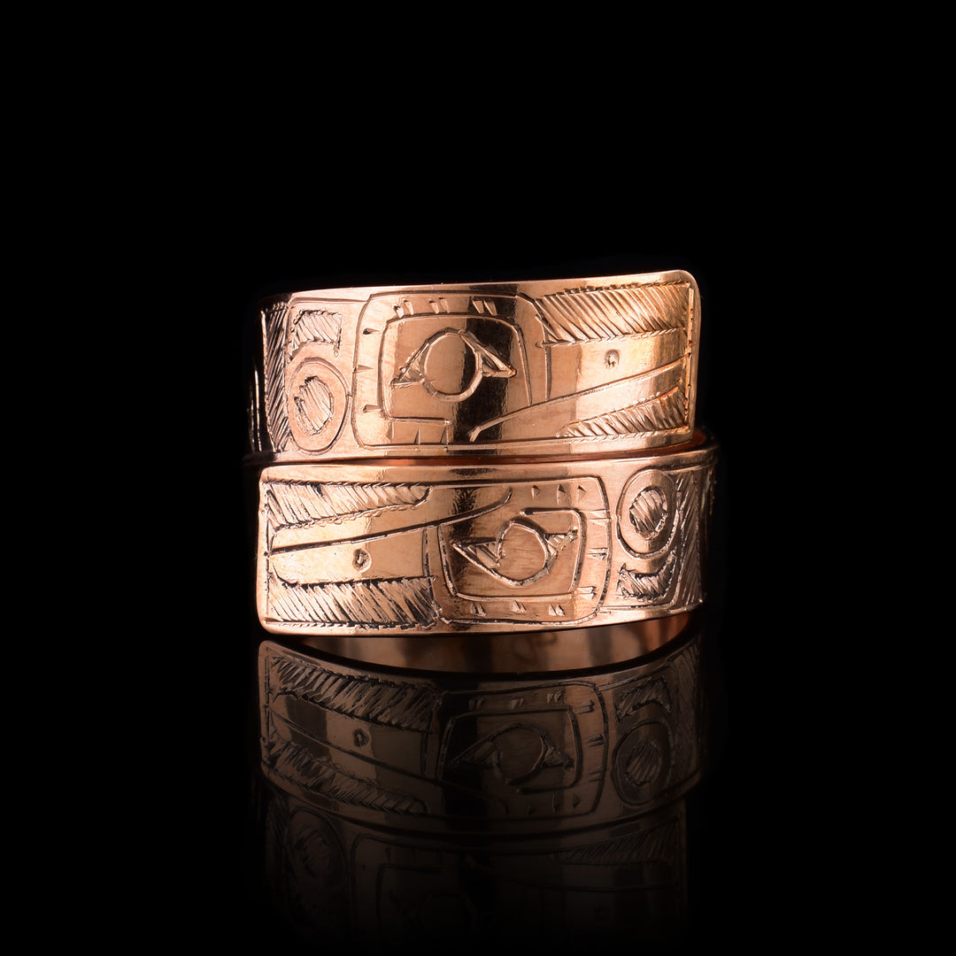 This copper wrap around ring has a single band that wraps around the finger twice. There is a depiction of the Hummingbird head at one end of the band and another on the other end. The depictions are done in a side profile. There are feather designs behind the back of its head.