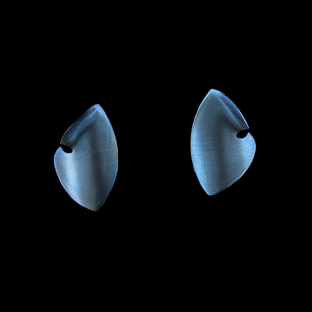 These titanium earrings studs are made from blue titanium and there are large and teardrop shaped. The studs curve to a point at both ends and there is a small cutout on the side of the studs.