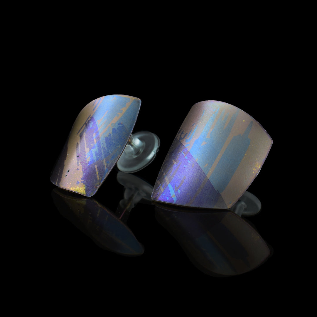 These colourful titanium earrings are convex and have an uneven, square shape. There are splashes of pink, purple and blue with paint brush designs made across the surface of the studs.