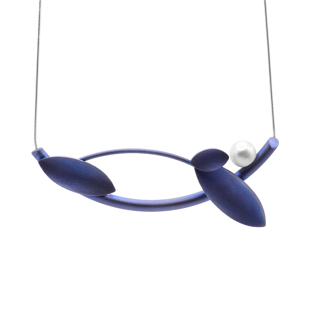 This leaf pendant necklace is made from blue titanium and has a horizontal pendant with a small chain attached onto either side of the pendant. There are two rods that curve against each other and represent branches. There are three different sizes of oval shaped leaves attached onto the branches. There is one freshwater pearl resting on one end of the pendant.