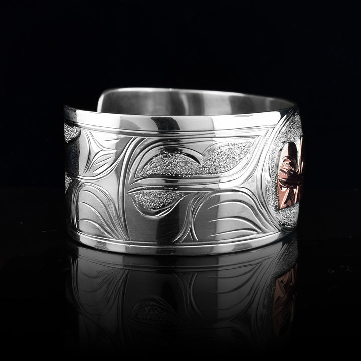 This sterling silver copper bracelet has a single, wide band with a gap in the back and the head of the Wolf is depicted in the center of it. The head is done in copper and at a side profile. On both sides of the band, there are carvings showing the body of the legend with its paws, claws and tail detailed in a side profile.