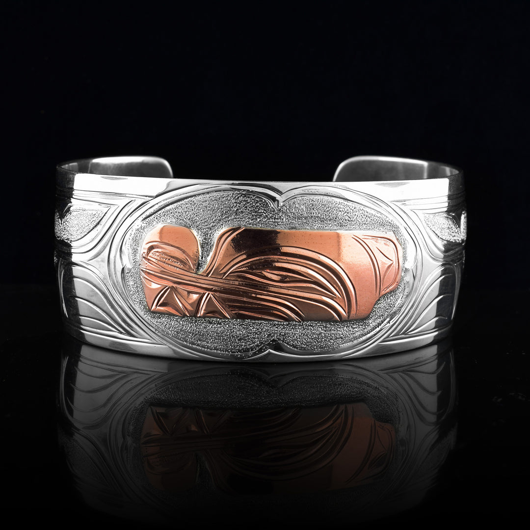 This sterling silver copper bracelet has a single, wide band with a gap in the back and the head of the Wolf is depicted in the center of it. The head is done in copper and at a side profile. On both sides of the band, there are carvings showing the body of the legend with its paws, claws and tail detailed in a side profile.