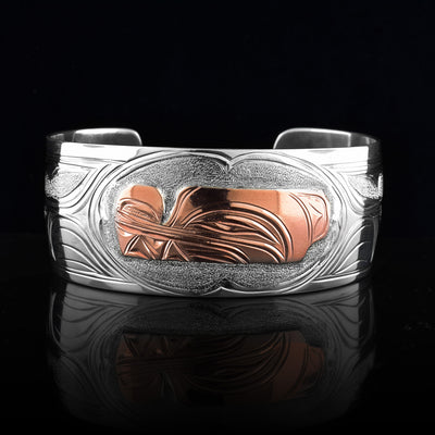 This sterling silver copper bracelet has a single, wide band with a gap in the back and the head of the Wolf is depicted in the center of it. The head is done in copper and at a side profile. On both sides of the band, there are carvings showing the body of the legend with its paws, claws and tail detailed in a side profile.