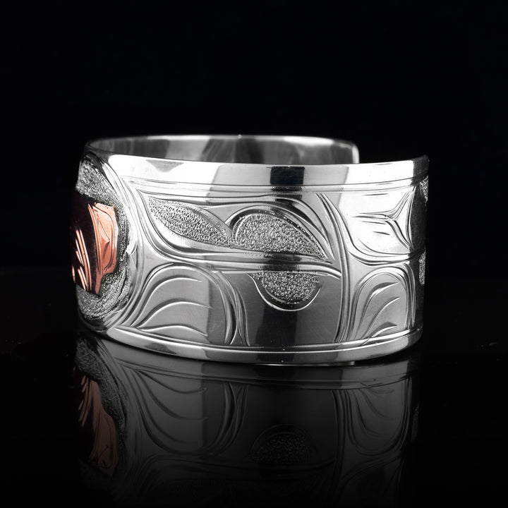 This sterling silver copper bracelet has a single, wide band with a gap in the back and the head of the Wolf is depicted in the center of it. The head is done in copper and at a side profile. On both sides of the band, there are carvings showing the body of the legend with its paws, claws and tail detailed in a side profile.