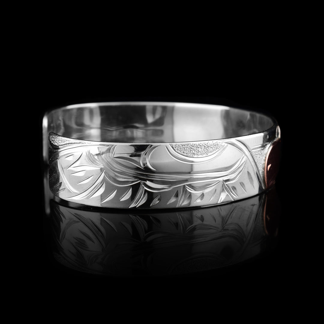 This sterling silver copper bracelet has a single band with a gap in the back and the head of the raven is depicted in the center of it. The head is done in copper and at a side profile. On both side of the band, there are carvings showing the wings outstretched with feather details.