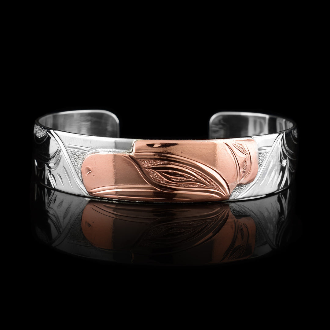This sterling silver copper bracelet has a single band with a gap in the back and the head of the raven is depicted in the center of it. The head is done in copper and at a side profile. On both side of the band, there are carvings showing the wings outstretched with feather details.
