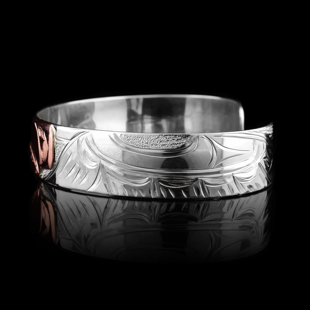 This sterling silver copper bracelet has a single band with a gap in the back and the head of the raven is depicted in the center of it. The head is done in copper and at a side profile. On both side of the band, there are carvings showing the wings outstretched with feather details.