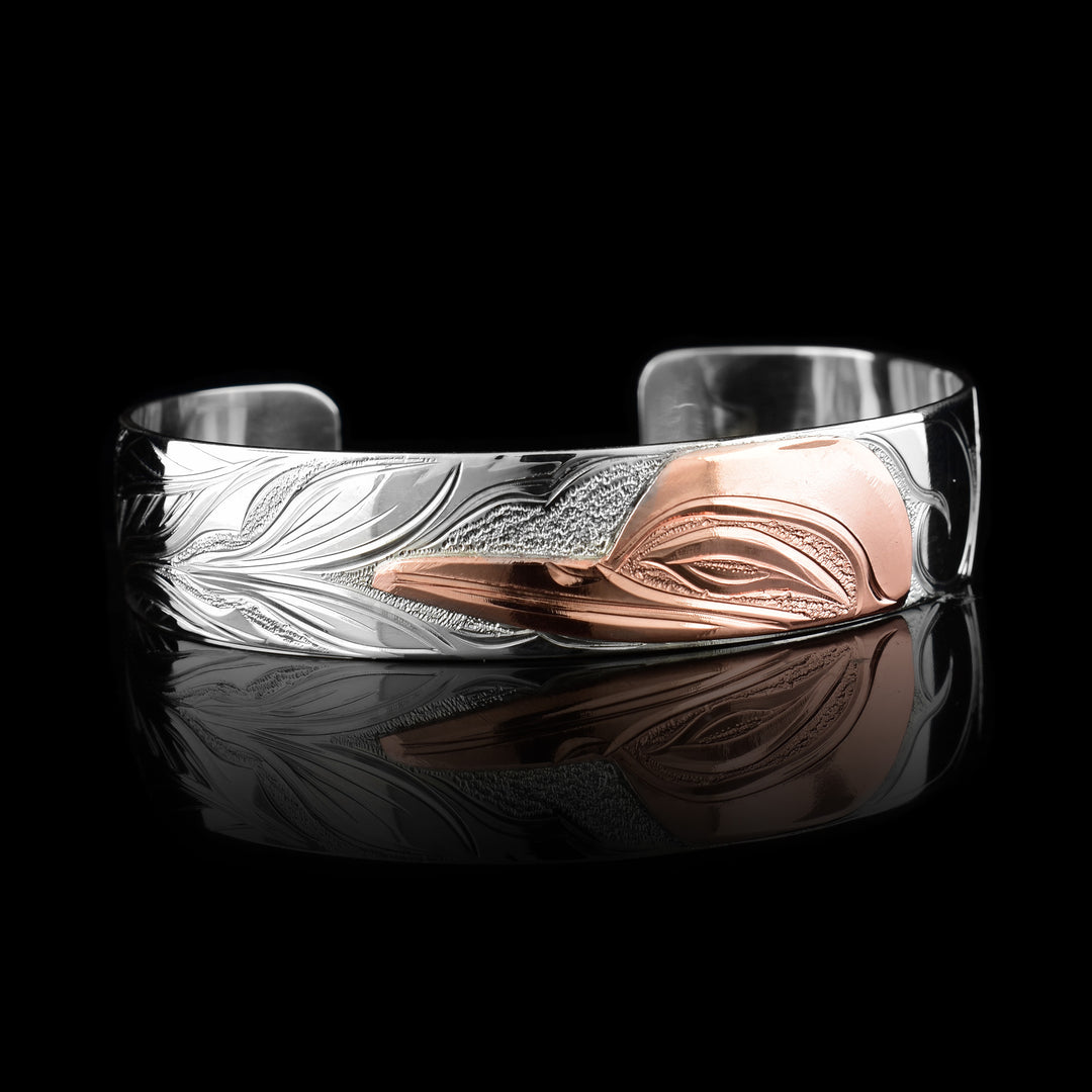 This sterling silver copper bracelet has a single band with a gap in the back. The head of the Hummingbird is done at a side profile using copper and there is a wing designs carved behind it on the band. On the other side there are floral design and its beak is reaching between two flower petals.