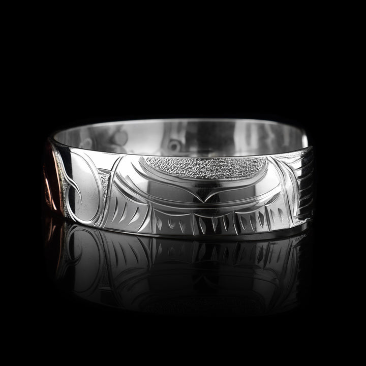 This sterling silver copper bracelet has a single band with a gap in the back. The head of the Hummingbird is done at a side profile using copper and there is a wing designs carved behind it on the band. On the other side there are floral design and its beak is reaching between two flower petals.