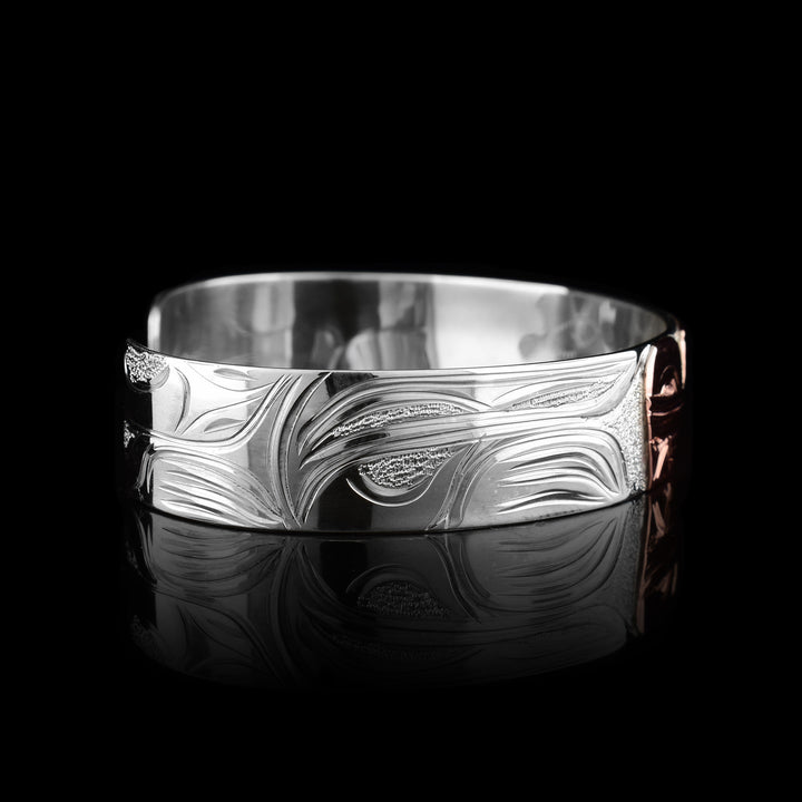 This sterling silver copper bracelet has a single band with a gap in the back and the head of the Wolf is depicted in the center of it. The head is done in copper and at a side profile. On both sides of the band, there are carvings showing the body of the legend with its paws, claws and tail detailed in a side profile.