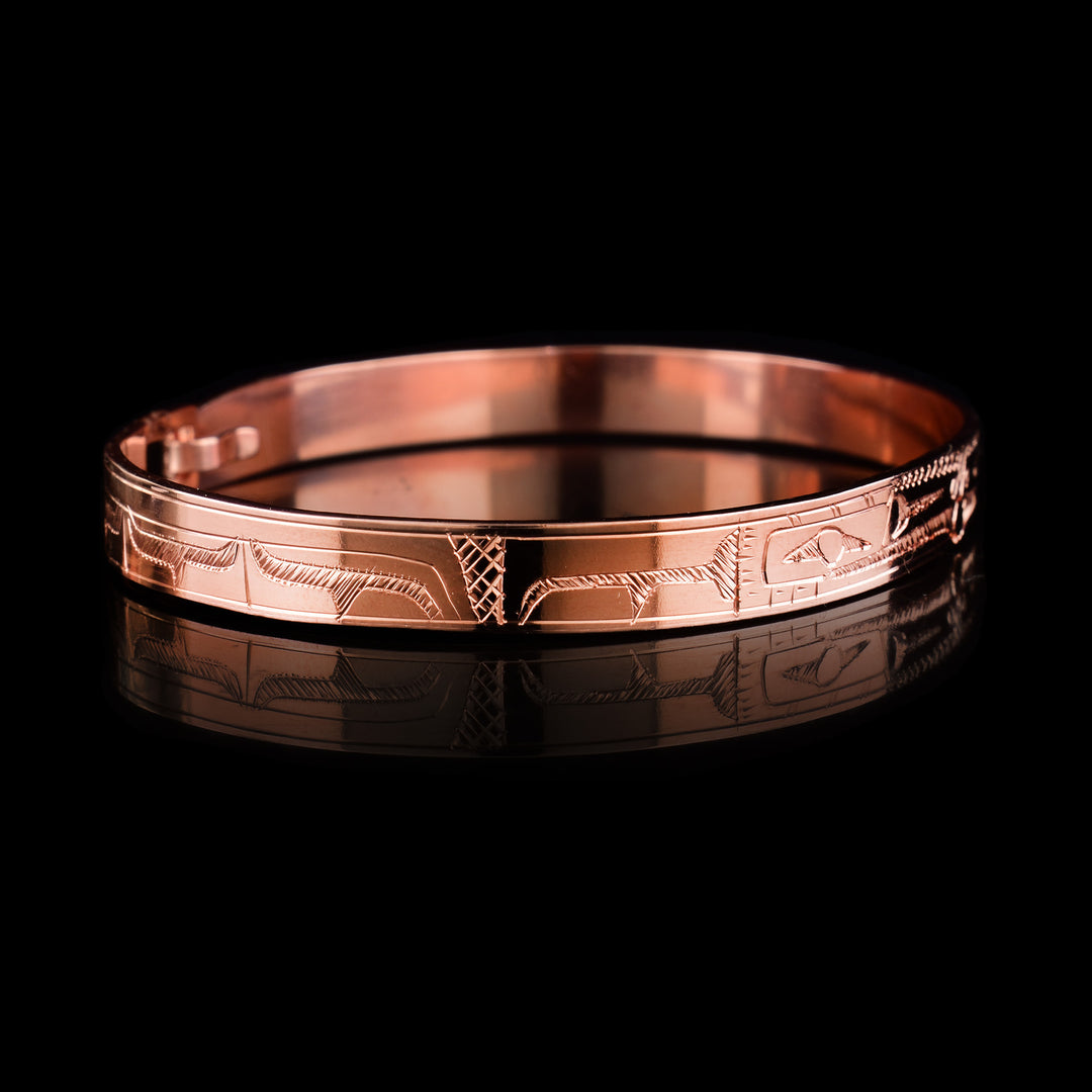 This Raven bracelet bangle has a thin, copper band with a clasp in the back. There are two Ravens carved at a side profile and their heads meet in the center of the band. There is a pearl that is held in their mouths and cross hatching designs in the background of the piece.