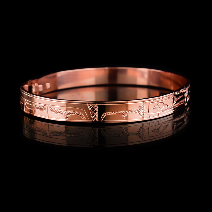 This Raven bracelet bangle has a thin, copper band with a clasp in the back. There are two Ravens carved at a side profile and their heads meet in the center of the band. There is a pearl that is held in their mouths and cross hatching designs in the background of the piece.