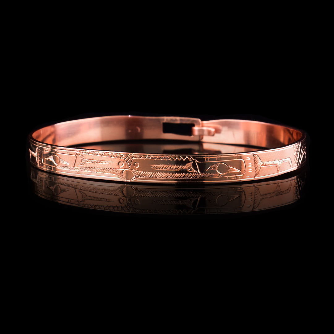 This Raven bracelet bangle has a thin, copper band with a clasp in the back. There are two Ravens carved at a side profile and their heads meet in the center of the band. There is a pearl that is held in their mouths and cross hatching designs in the background of the piece.
