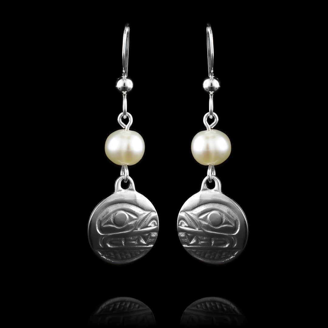 These dangling pearl earrings silver have small, circle hangs made from sterling silver. Below the hooks is a single, white pearl with the hangs dangling from them. On the hangs, the head of the Bear is shown at a side profile with its eye, nose and teeth detailed. There are cross hatching designs in the background of the portrait.