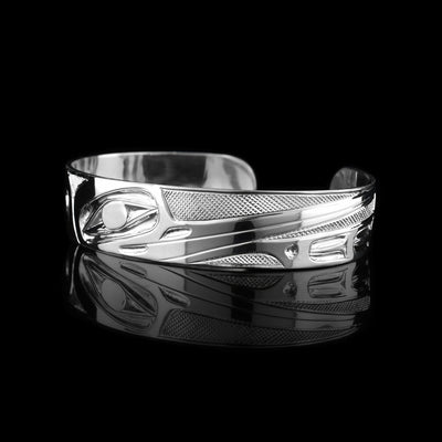 This Hummingbird bangle bracelet has a single, sterling silver band with a gap in the back. The head of the Hummingbird is shown in the front at a side profile. The head is large and stretches across most of the band. On either end of the band are wing designs and there are cross hatching designs in the background of the scene.
