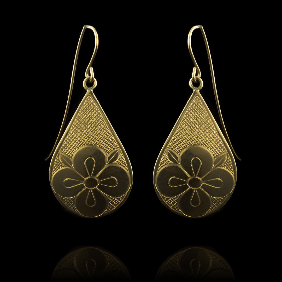 These 14K Gold flower drop earrings have teardrop shaped hangs with a flower carved into the bottom of the teardrop There are cross hatching designs in the background of the scene.