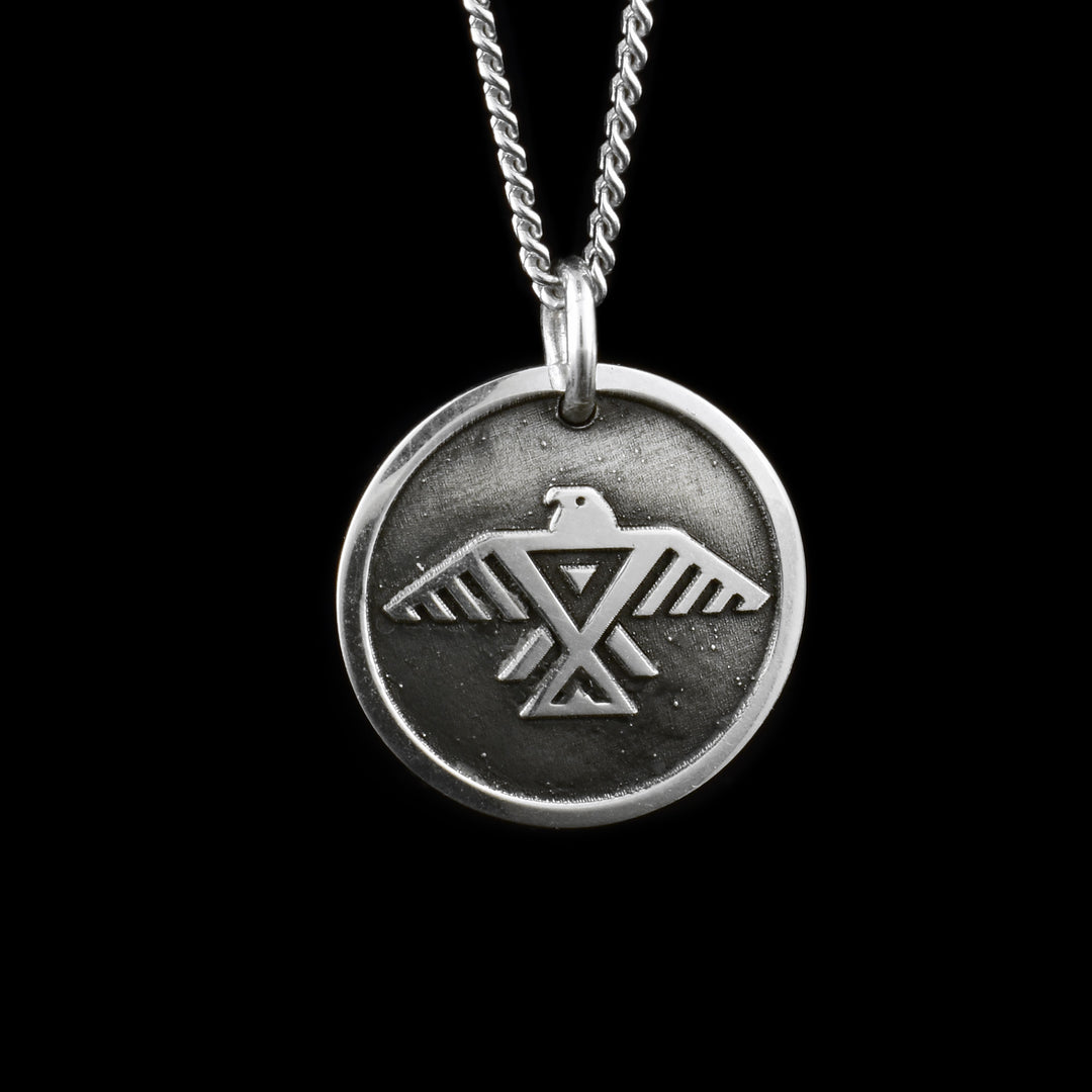 This sea turtle pendant necklace has a small, circle shape and is made from sterling silver. There is a tribal, like depiction of the Thunderbird with its wings outstretched and head to the side.