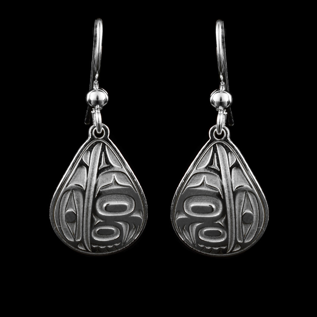 These teardrop dangle earrings have wide, round and teardrop shaped hangs made from sterling silver. Half the piece has deep markings representing the head of the Raven and the other half is a wing design with feather details.