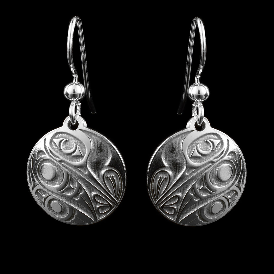 These small dangle earrings have circle shaped hangs made form sterling silver. There is a depiction of the Hummingbird cast into the hangs at a side profile. The beak is facing down and there is one, large eye on the head. its wing and tail are tucked underneath is and its beak is sticking into a flower.