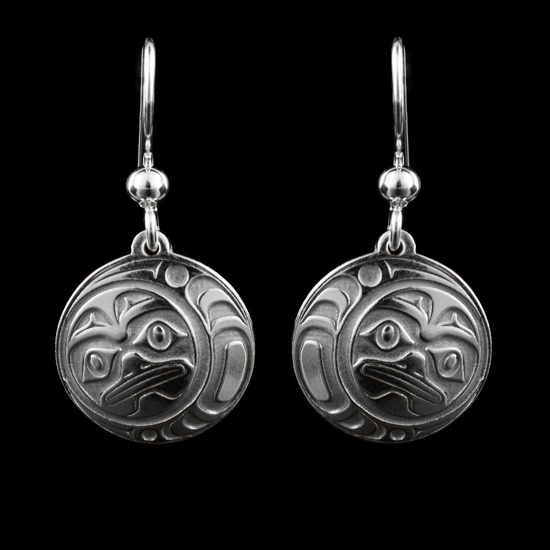 These Moon dangle earrings have circle shaped hangs made from sterling silver. There are depictions of the full moon cast into the hangs with eyes, eyebrows, nose and mouth. There are crescent designs on the side of the hangs around the legend.