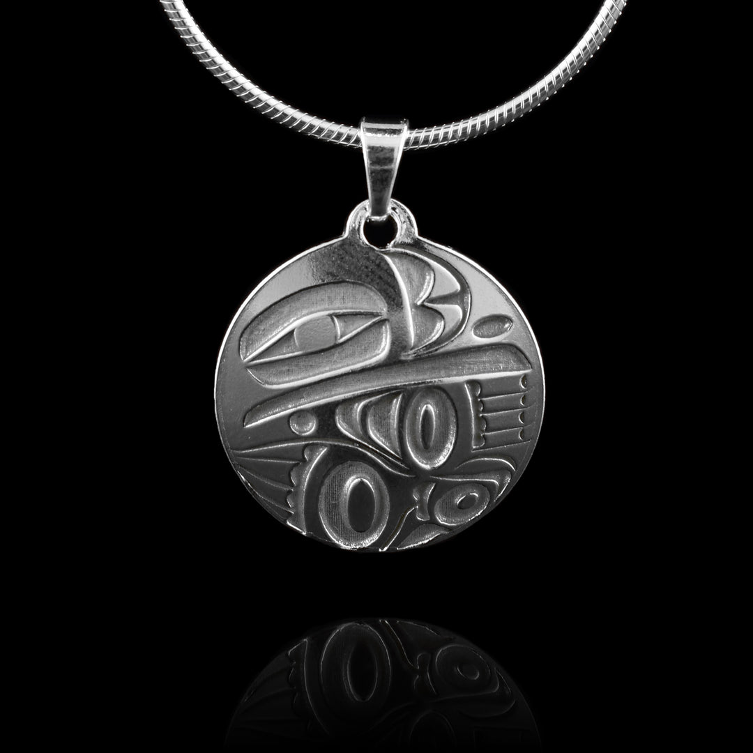 This Raven silver pendant has a circle shape made from sterling silver. There is a depiction of the Raven cast into the pendant at a side profile. The top half consists of the eye, beak and nose and below is a wing design with feather details included.