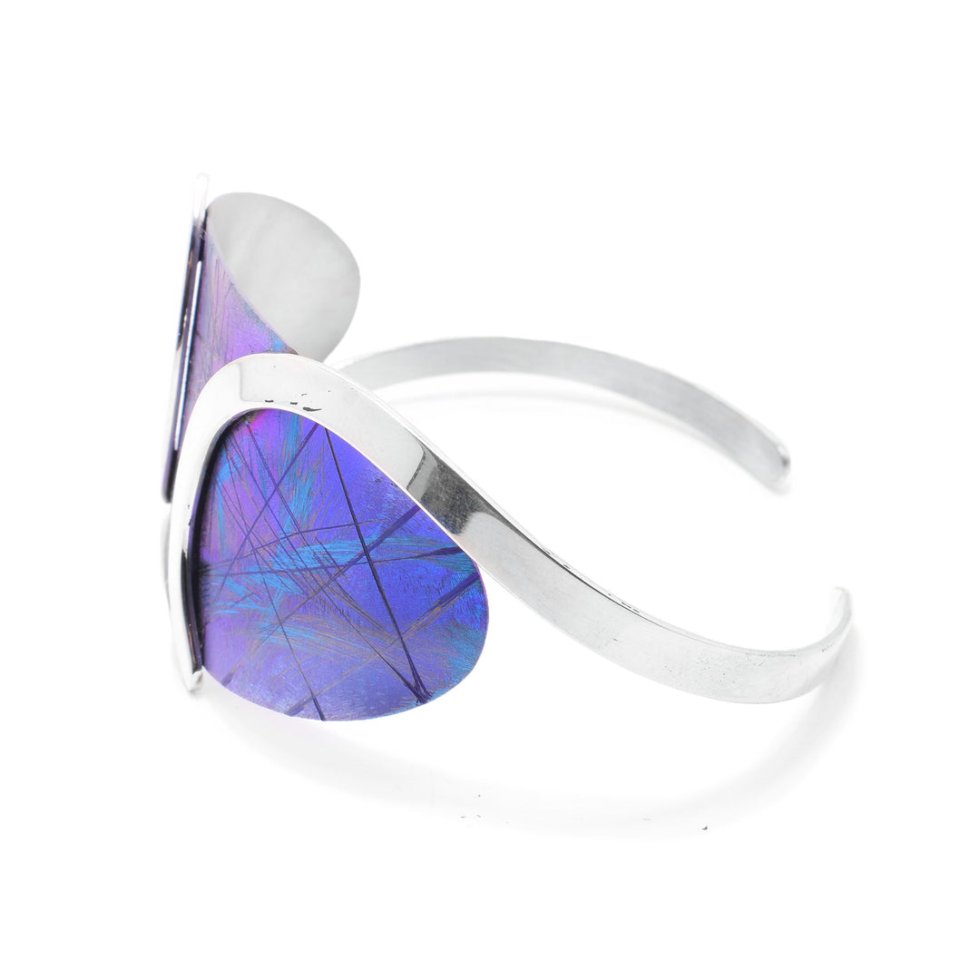 This blue titanium bracelet has a wide, oval piece at the top with a blue color and purple, line designs on it. This piece is held with swirling bands made from sterling silver. There is a gap between the silver bands at the bottom.