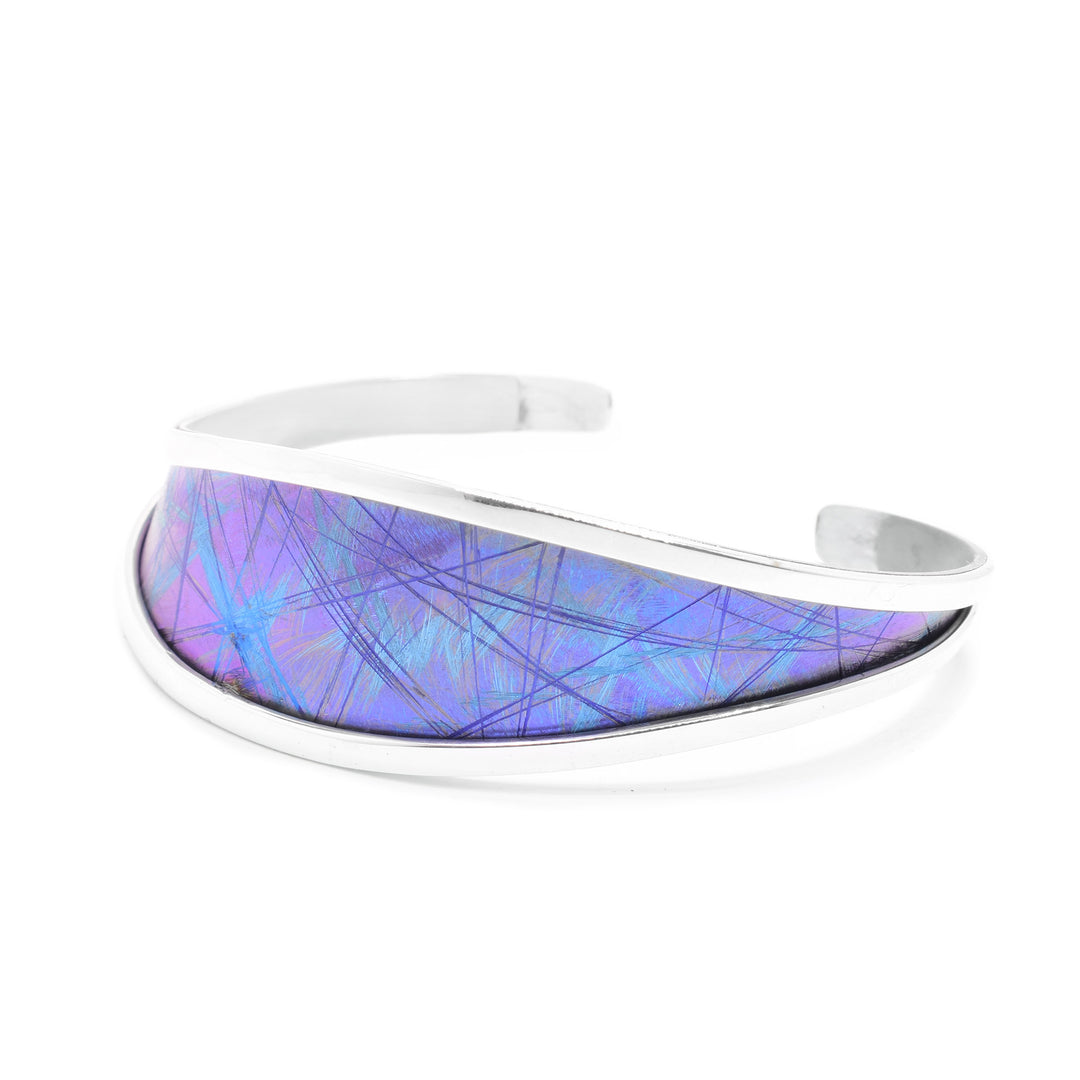 This titanium bangle bracelet has a wider top with a titanium piece held between sterling silver bands. The piece tapers towards the back into just the silver bands and there is a gap. There are blue and purple designs made in the titanium by anodizing the material