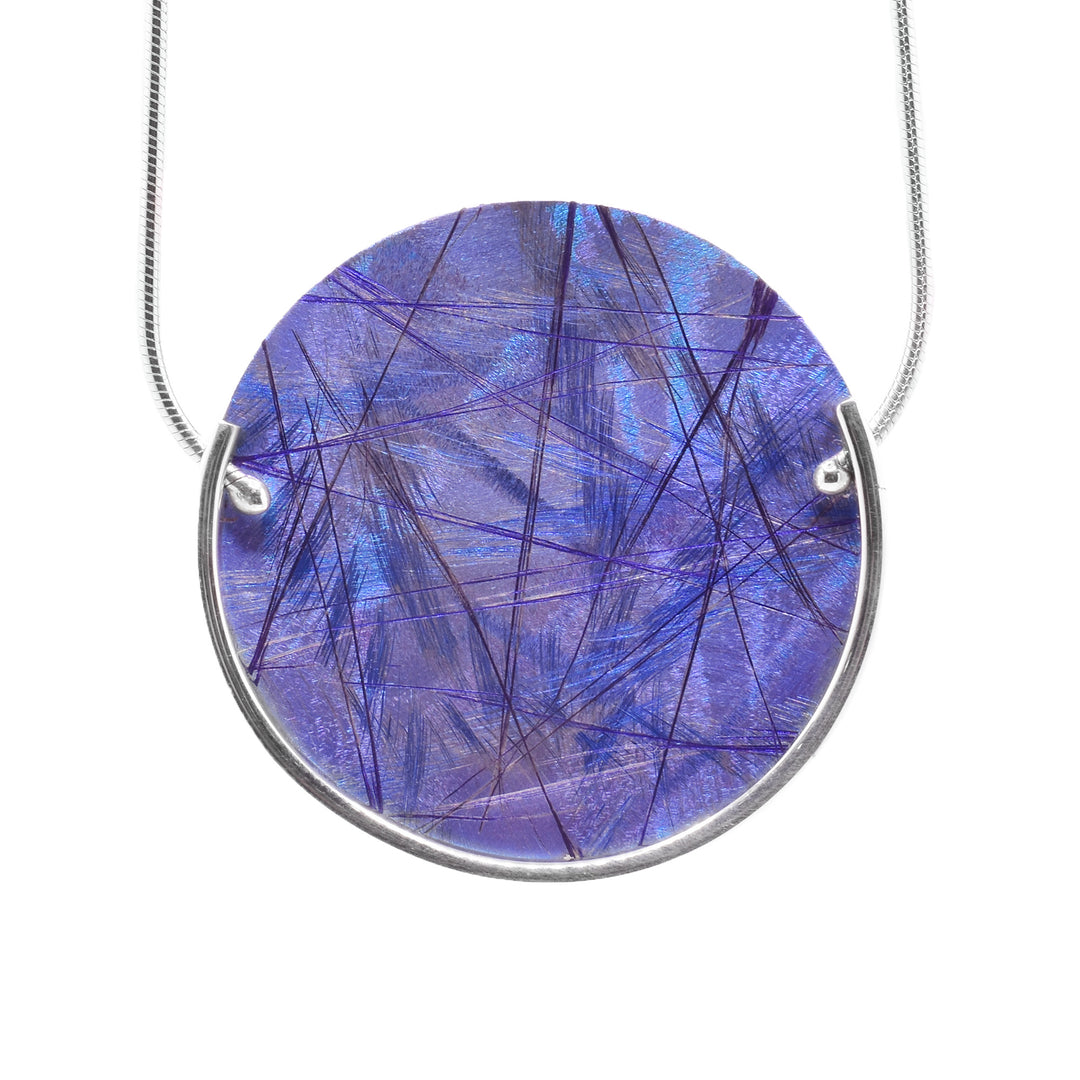 This titanium pendant necklace has a circle shape and has a blue color with purple designs on it. The colors are achieved by an anodizing the pendant. There is a sterling silver wire running around the bottom half of the circle pendant.