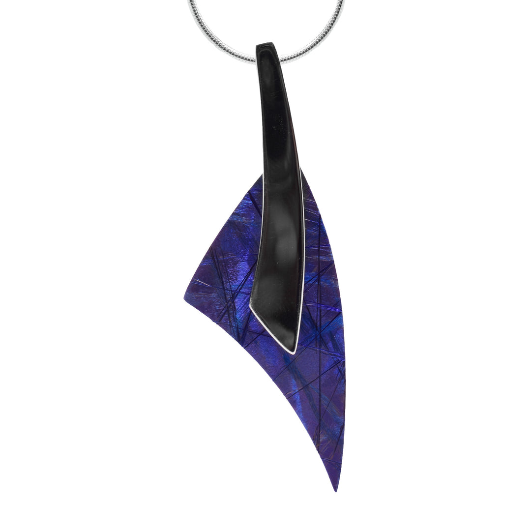 This long pendant necklace has a pendant with a long, curved band made from sterling silver dropping down. Half way down this band, the is a sharp, triangular piece of anodized titanium that is blue with purple designs.