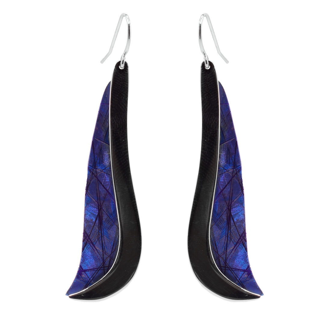 These titanium drop earrings have long, wavy hangs that are wider at the bottom than the top. One end is line with a sterling silver band that follows the edge of the hangs and the other side is made from anodized titanium. The titanium has a blue color with purple design on its surface.