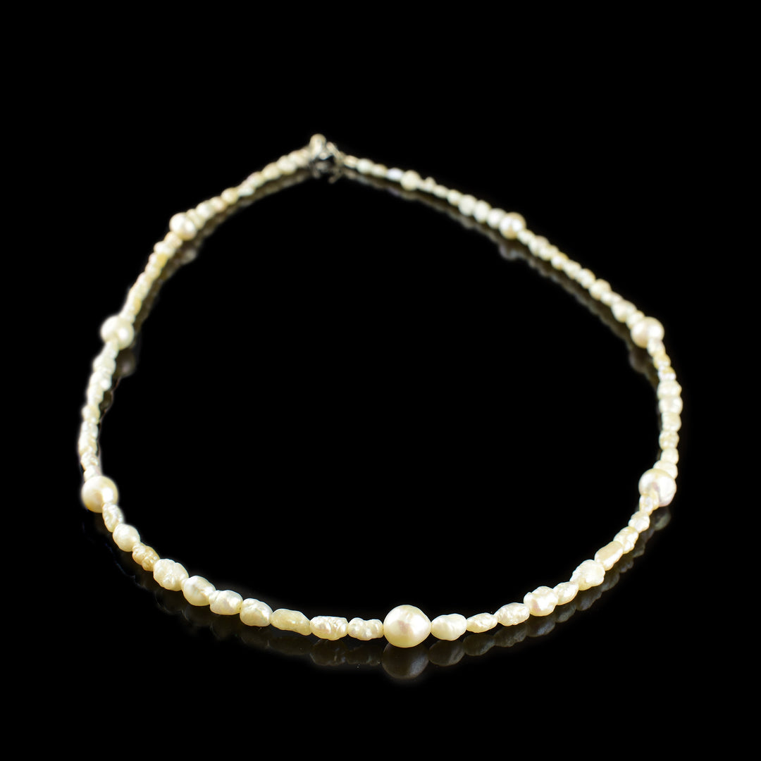 This pearl bead necklace consists of small, irregularly shaped pearls with a few larger ones place around it.