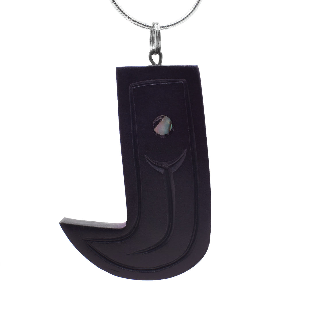 This Bear claw pendant is carved out of argillite stone and drop downs with a sharp curve at the bottom. The end is sharp and there are details carved into the piece outlining the claw and designs. There is a small piece of abalone shell set at the top of the pendant.