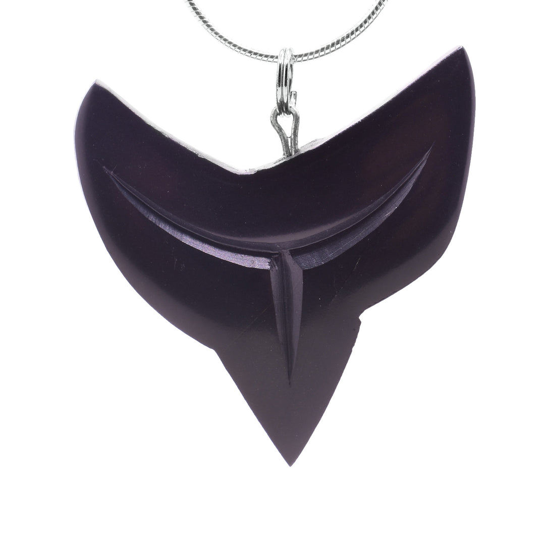 This shark tooth pendant is large and carved from argillite stone. There is a large, crescent shape with its points facing up and a sharp tooth shape extending from the bottom. There are carved lines on the piece detailing the tooth.