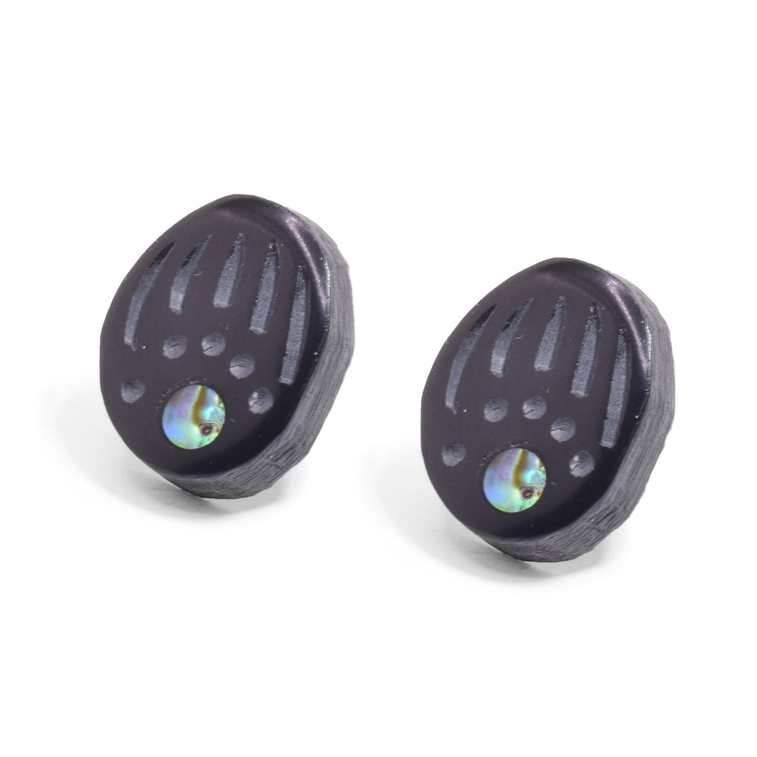 There abalone stud earrings are thick, oval shaped and made from argillite stone. There are carvings on their surface detailing a bears paw with long claws. There is an abalone shell set where the "palm" of the paw would be.