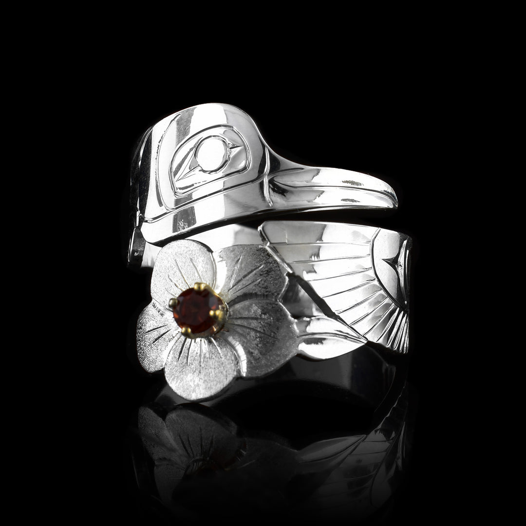 This Hummingbird ring is made from sterling silver and has a single band that wraps around the finger twice. There are carvings on the surface of the piece depicting the Hummingbird. The head is on the top and the wing with a rose at the bottom. There is a garnet gem held in the center of the flower.