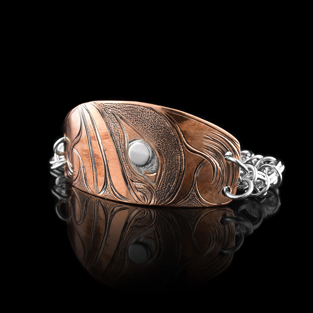 This chain bracelet with plate has a chunky, sterling silver chain with multiple hoops linked each other. There is a wide, oval shaped plate in the top of the chain. The plate is capper and has a carving depicting the Orca among many waves. The eye of the Orca is sterling silver.