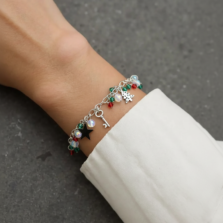 Bracelet with charms on a wrist against a neutral background.

Christmas Charm Bracelet, with sleighs, stars and Christmas tree decorated with Christmas coloured beads around a sterling silver chain.