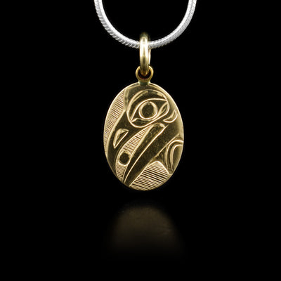 Pendant features side-view of raven head with ball in mouth. Finely carved lines in background. 14K yellow gold.